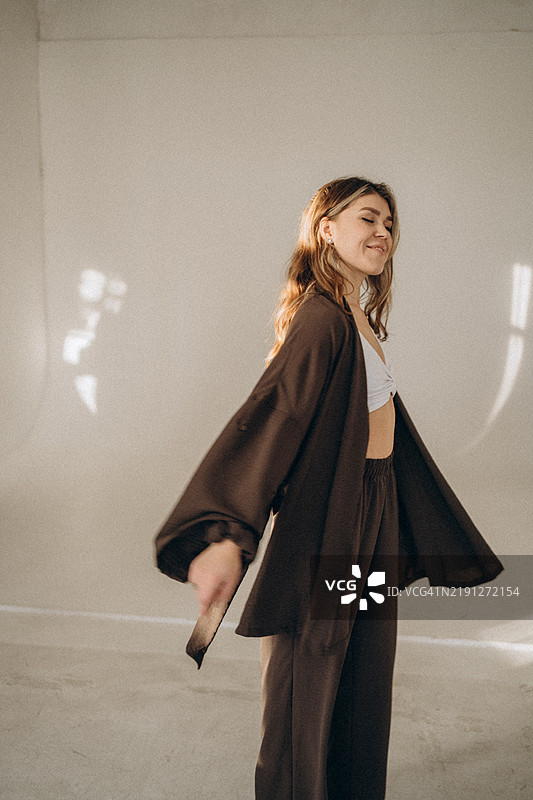 时尚模特穿着棕色服装在自然光下的摄影棚中摆姿势图片素材