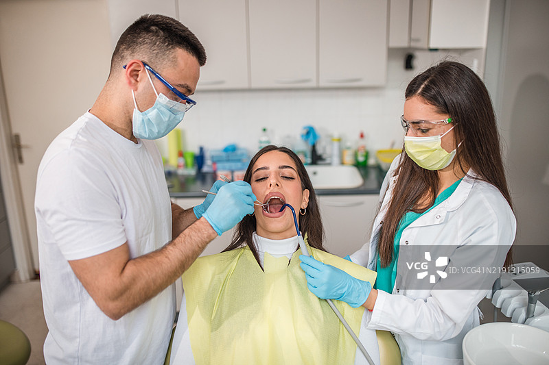 专注的牙医和他的牙科助手正在为病人治疗牙齿图片素材
