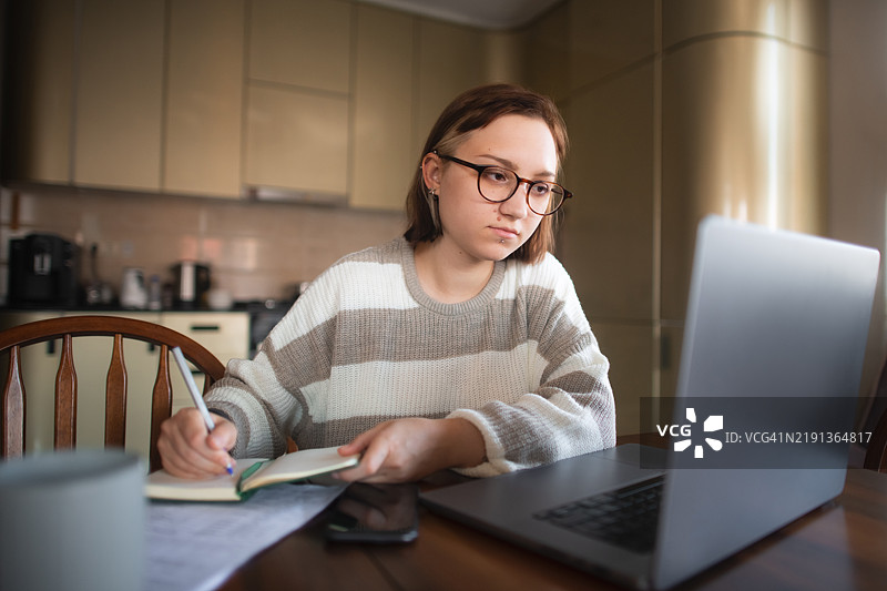 年轻女性在家中使用笔记本电脑审阅银行或财务文件/报表图片素材