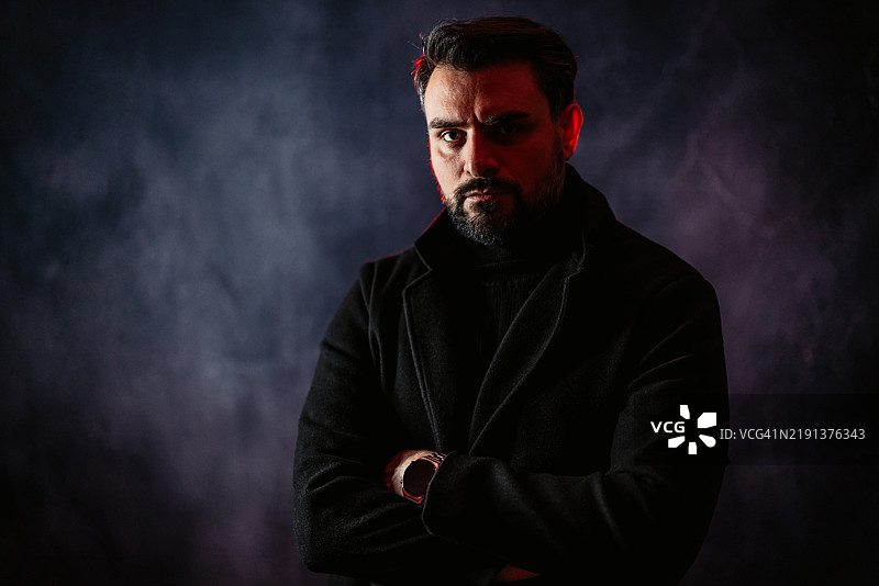 严肃的中年男子站在灰色背景下的红光照射下图片素材