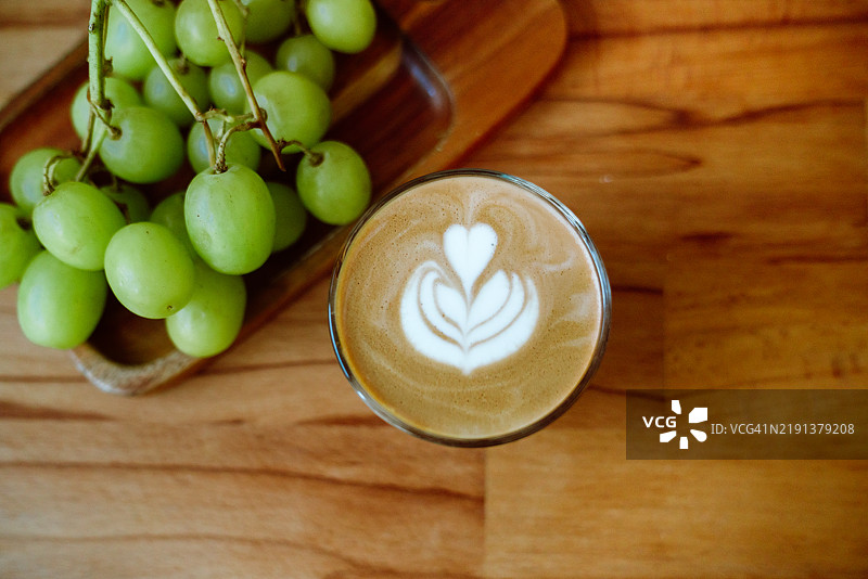 自制咖啡拿铁的俯视图，旁边放着一串白葡萄，摆在木盘上图片素材