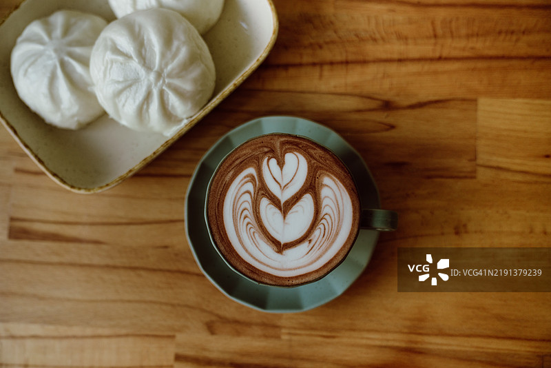 陶瓷盘上摆放着自制热巧克力拿铁和三个中式蒸包的俯视图图片素材