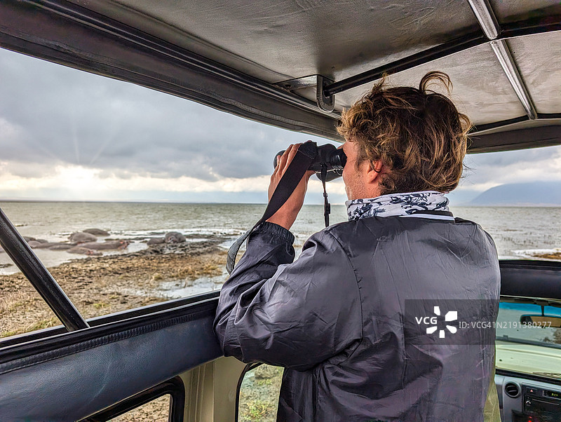 游客在坦桑尼亚恩戈罗恩戈罗保护区的 safari 车上通过望远镜观察河马，周围是壮丽的风景和生机勃勃的野生动物。图片素材