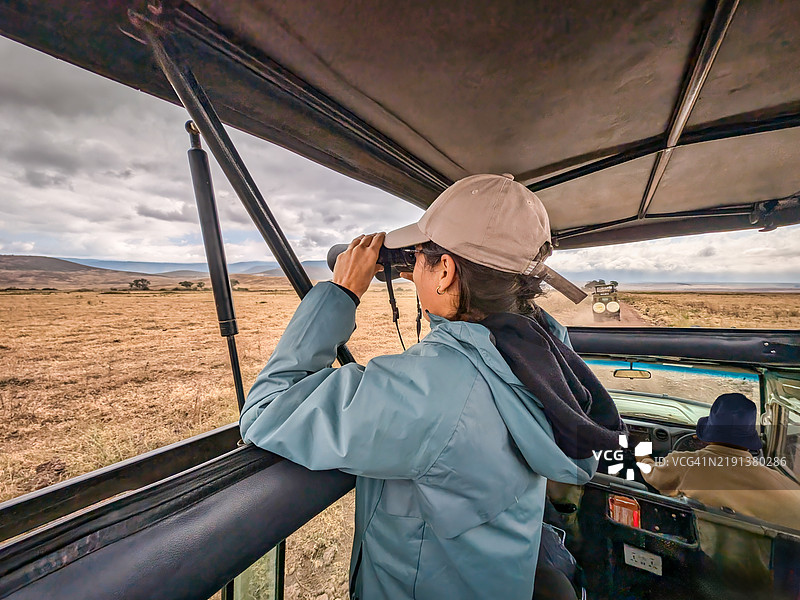 女性旅行者在野生动物园车上使用望远镜，扫描坦桑尼亚恩戈罗恩戈罗保护区广袤草原上的野生动物。图片素材