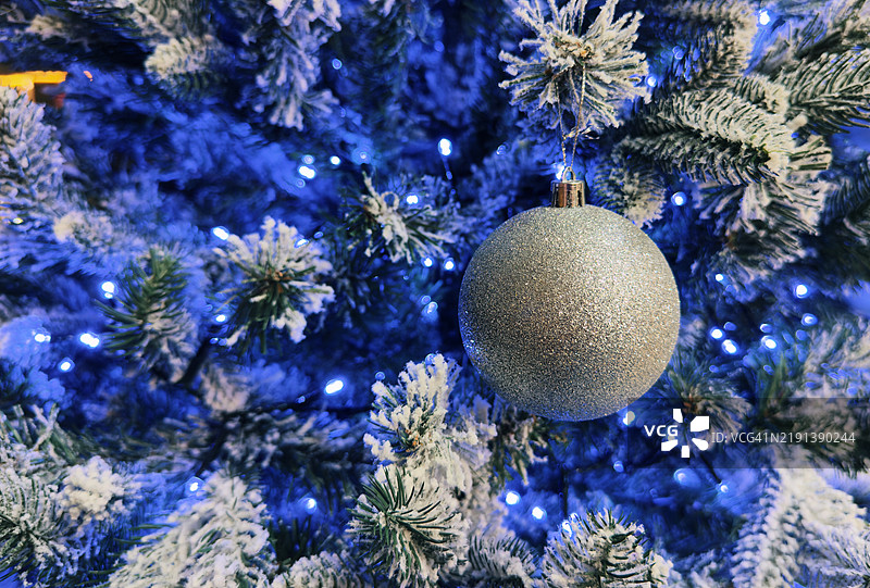 银色闪亮的圣诞装饰品挂在圣诞树上，周围有蓝色灯光。图片素材