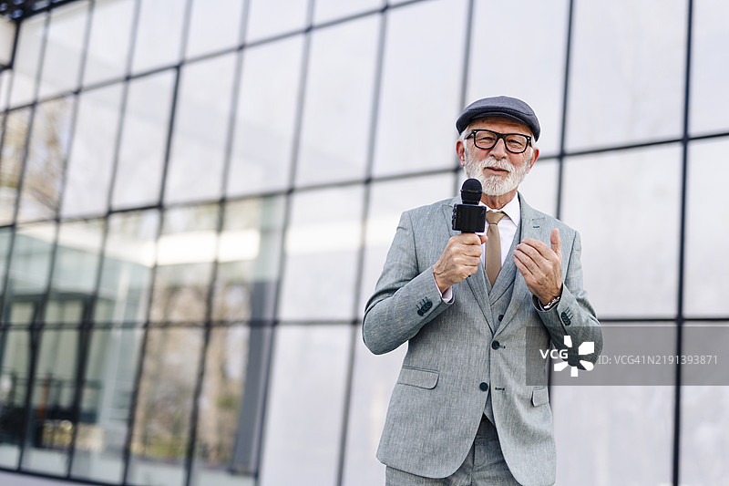 老年男性新闻记者在直播中。户外电视记者正在播报新闻。图片素材