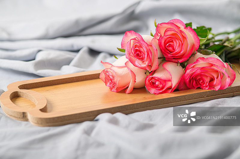 粉色玫瑰放在木托盘上，背景是柔软的布料图片素材