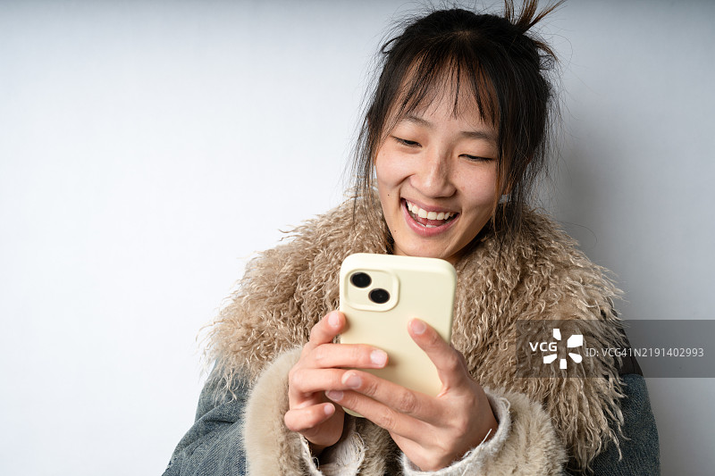 一位年轻的亚洲女性在白色背景前使用智能手机。图片素材