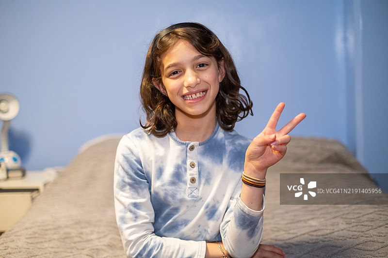 年轻的青春期女孩微笑着，望向镜头，做出和平手势。图片素材