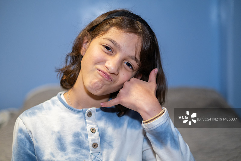 年轻的青春期女孩看着镜头，手势做出打电话的动作图片素材