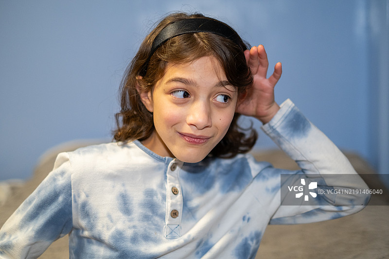 年轻的青春期前女孩把手放在耳边，专心倾听。图片素材