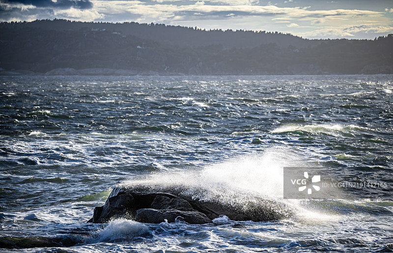 海浪猛烈地拍打着岩石，水花在空中弥漫，如同雾气。图片素材