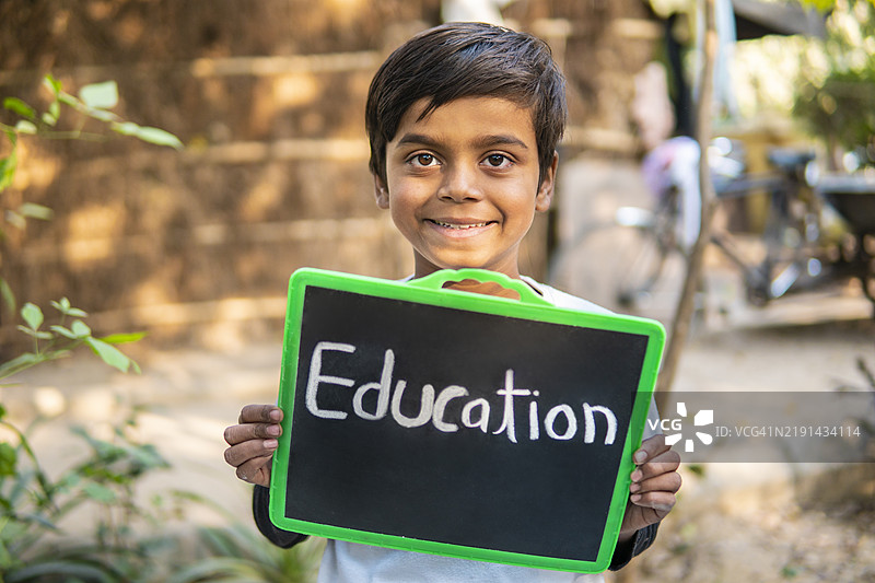 微笑着拿着黑板的印度小男孩肖像。图片素材