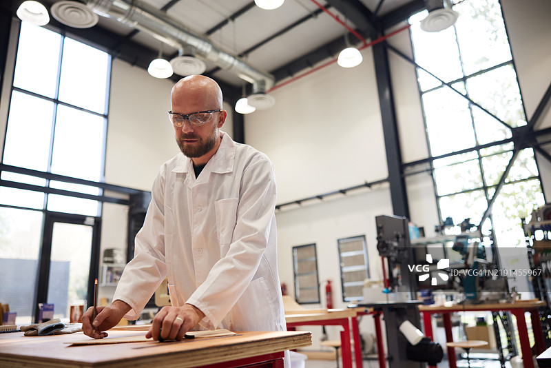 在木工车间，一位工匠正在木板上精确测量。图片素材