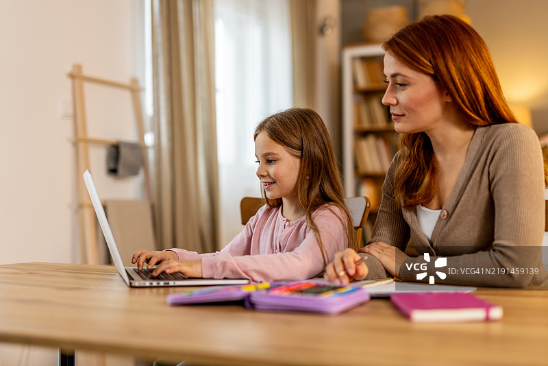 母亲在家中帮助年轻女儿使用笔记本电脑进行在线学习图片素材