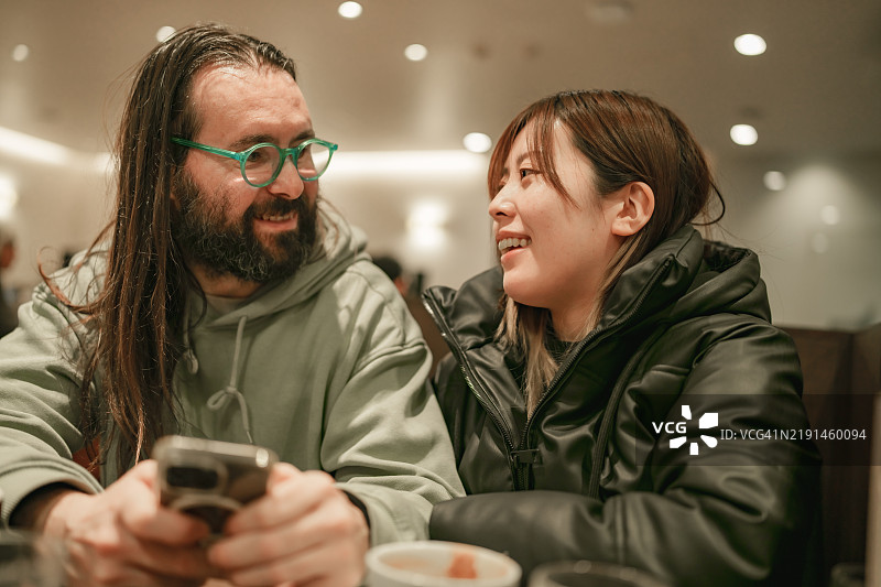 多元种族的情侣在咖啡馆使用手机。图片素材