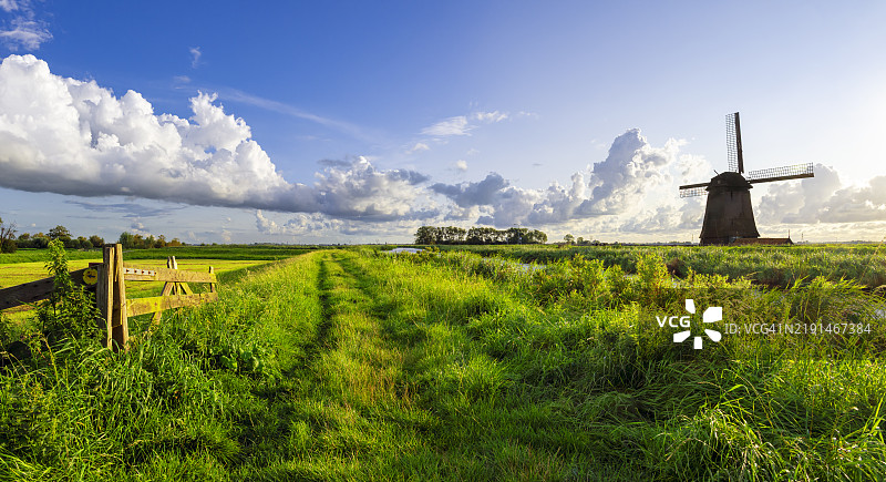 典型的荷兰风景，位于荷兰斯赫梅霍恩，沿着运河有一条小弯曲的堤坝和一座风车，天空部分多云。图片素材