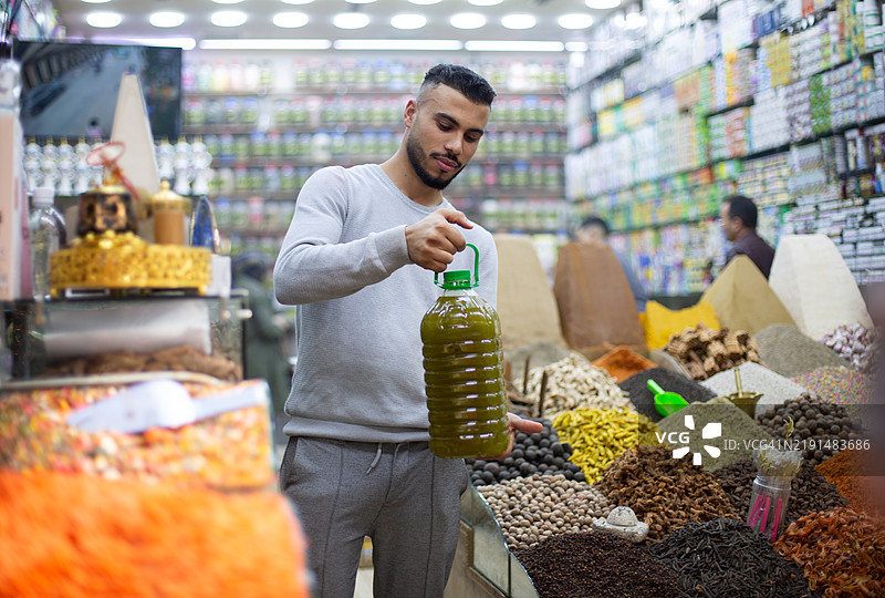 年轻男子在草药店里拿着一瓶橄榄油图片素材