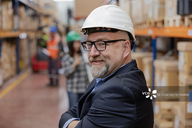 仓库中微笑着看向镜头的男性经理，双臂交叉，展现成熟的职业形象。图片素材