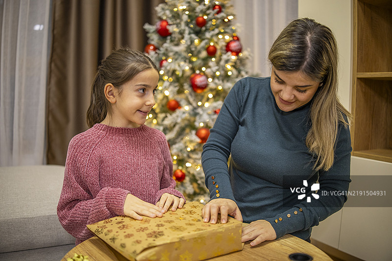 母亲和女儿一起在家中的圣诞树旁包裹和装饰圣诞礼物。图片素材