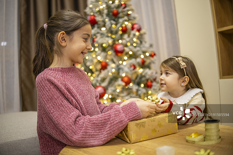 可爱的姐妹们在圣诞树前为家人装饰圣诞礼物。图片素材