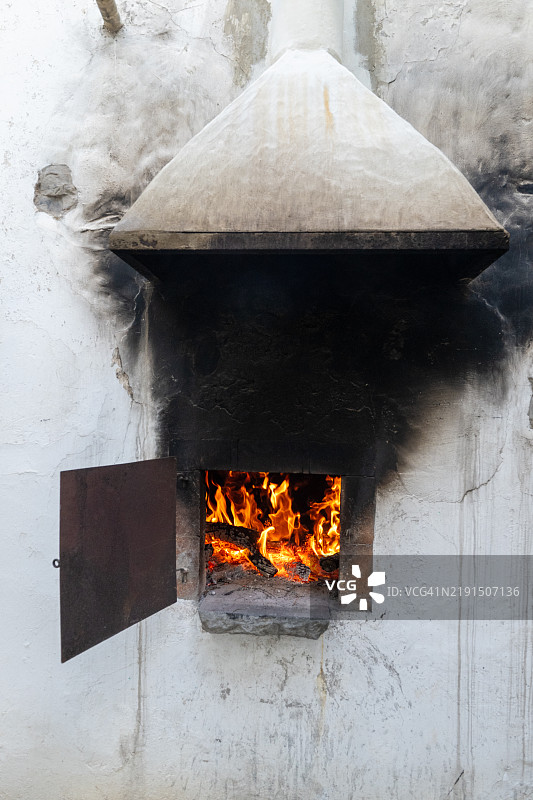传统木火烤炉中的火焰燃烧，嵌入白色粉刷的墙壁中图片素材