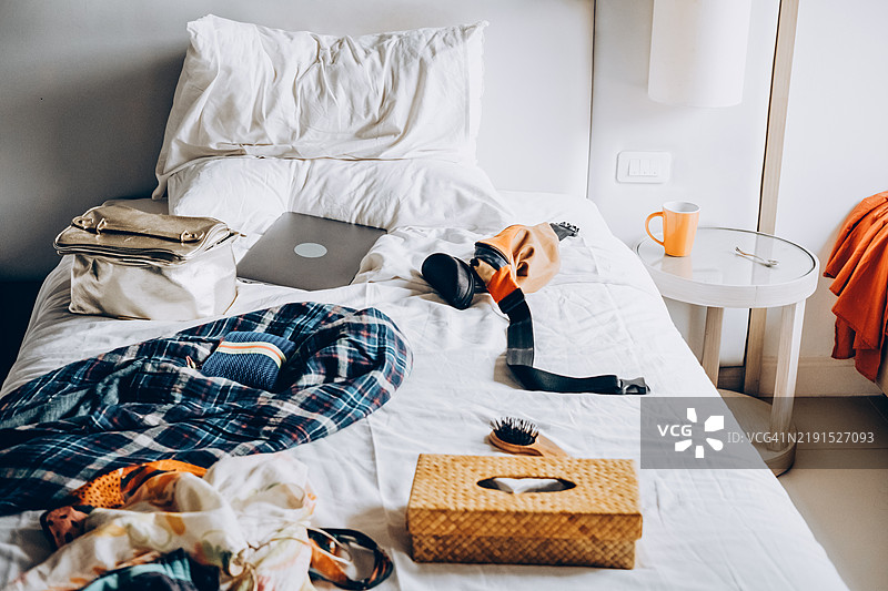 房间里一片混乱。床上有女性衣物和电脑。图片素材