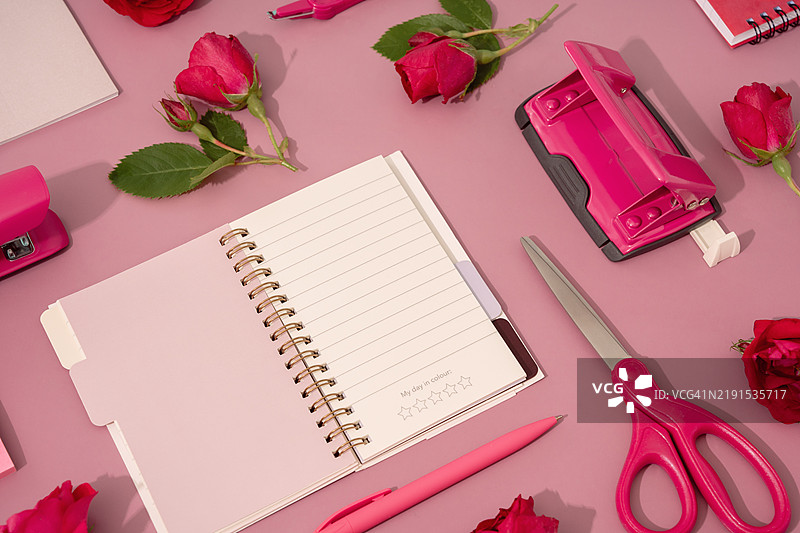红玫瑰与文具、模拟日历和记事本在粉色背景上图片素材