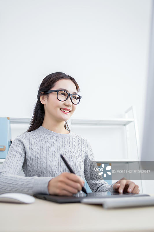 亚洲女性坐在桌子前使用绘图板工作图片素材