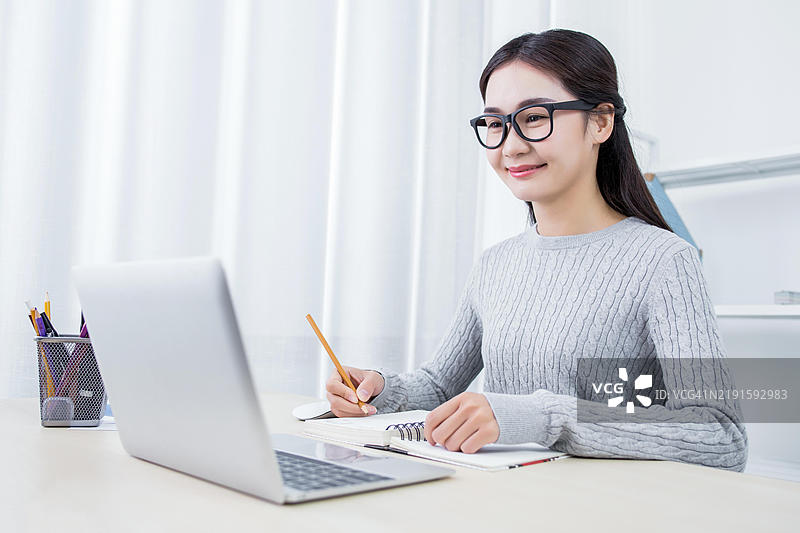亚洲女学生在使用笔记本电脑并做笔记，在线学习。图片素材