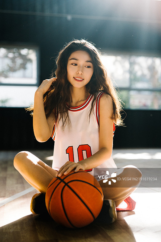 身穿白色篮球制服的美丽亚洲年轻女性在篮球场上手持篮球图片素材