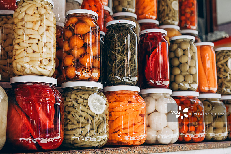 市场桌子上玻璃罐中的罐装蔬菜特写。自制蔬菜腌制品。图片素材