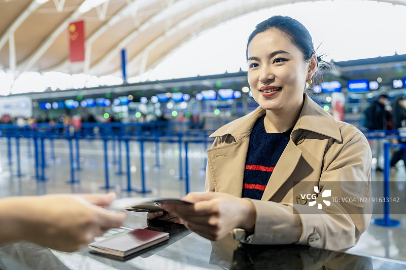 中年亚洲女性在航空公司值机柜台办理护照通行手续。图片素材