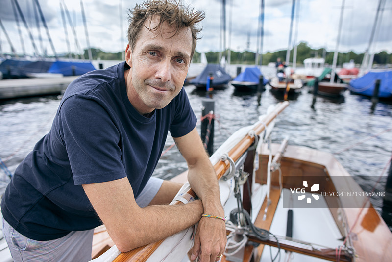自信的男人倚靠在码头的帆船上肖像图片素材