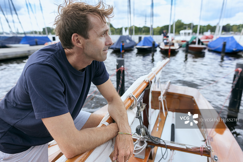 男子靠在码头的帆船上四处张望图片素材