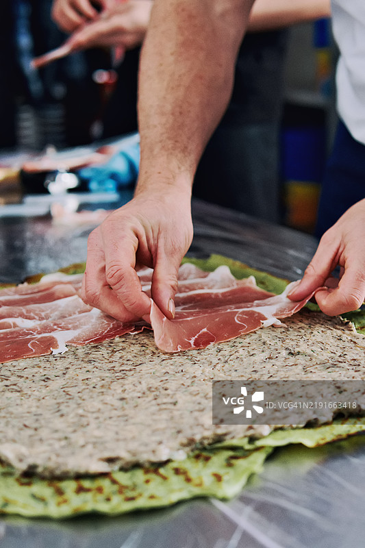 厨师在餐厅厨房将薄片的意大利火腿放在绿色叶子或面团层上。手工食品准备过程，烹饪或餐饮环境。图片素材