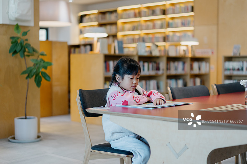 小女孩在图书馆的桌子上看书图片素材