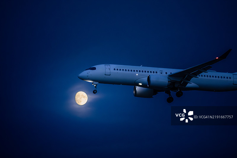 在黑暗的天空中降落的飞机与明亮的月亮图片素材
