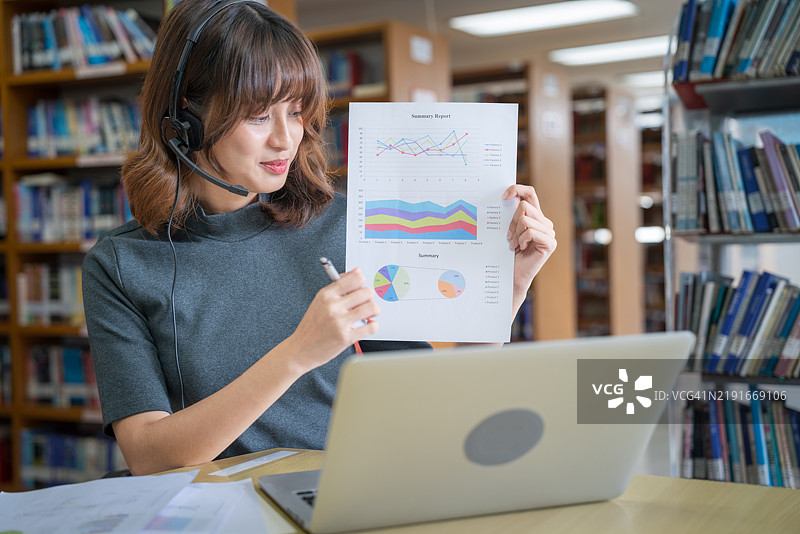 亚洲女性学生在图书馆通过电脑笔记本与老师进行视频会议，回归校园教育知识，大学概念。年轻女性在工作并使用电脑笔记本。图片素材