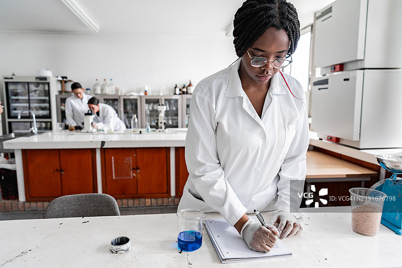实验室里，一位女科学家正在笔记本上做注释。图片素材