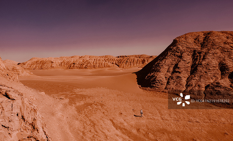 一名男子在伊朗的达什特-鲁特沙漠的广袤中行走。图片素材