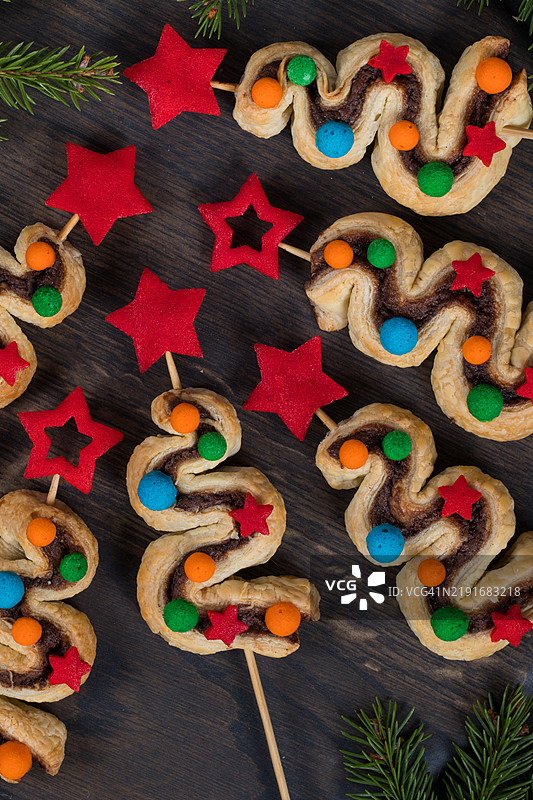 圣诞甜点。酥皮蛋糕，内含巧克力酱和肉桂，插在木棍上。装饰有红色星星和彩色球形玩具。放在木板上。深色背景。俯视图。特写。图片素材