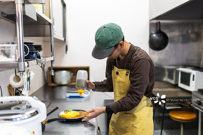 男子在餐厅为一盘咖喱做最后的修饰图片素材