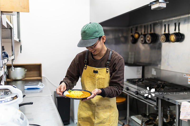 男子在餐厅为一盘咖喱做最后的修饰图片素材