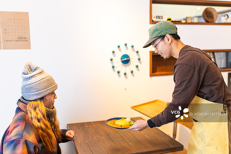 年轻男子在咖啡馆为顾客端上咖喱饭。图片素材