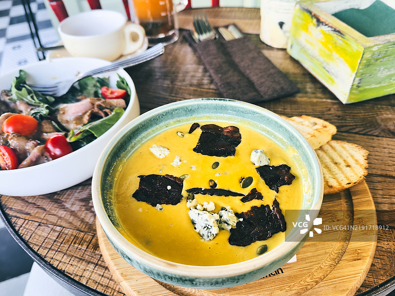 美味的南瓜汤配沙拉和手工面包，摆放在木桌上图片素材