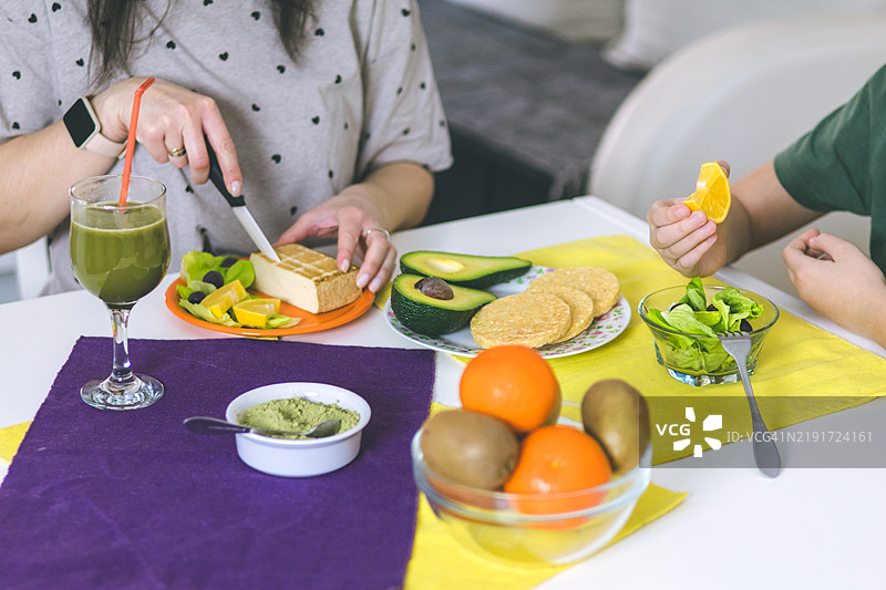 母亲和儿子在家中享受准备健康早餐的时光。早餐的超级食品成分包括螺旋藻、熏豆腐、鳄梨、生菜、米饼和水果。图片素材
