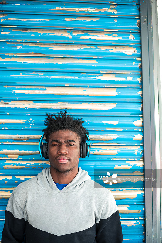 年轻黑人男孩佩戴耳机的肖像，背景为蓝色金属门。图片素材