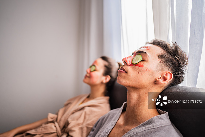 年轻男子在家卧室里戴着面膜，眼睛上放着黄瓜片，和妻子在一起。图片素材