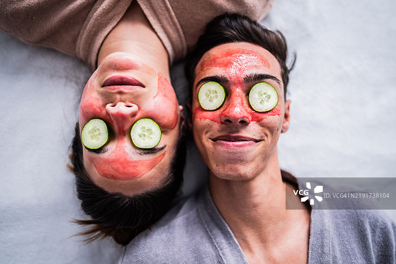 年轻情侣在家卧室里戴着面膜，眼睛上放着黄瓜片。图片素材